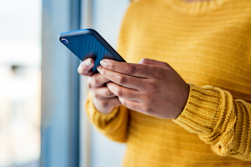 Eine Person in einem gelben Pullover tippt eine Instagram-Beschriftung mit einem Wort in ein Smartphone. 