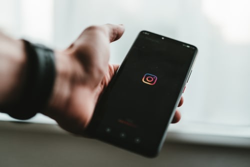 Person holding black smartphone with Instagram icon in the middle of the screen. 