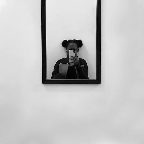 Photo en noir et blanc d'une jeune femme prenant un selfie devant un miroir.