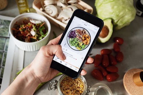 Person taking a photo of a salad for posting on Instagram with the hashtag #food. 