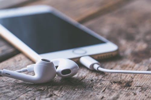 Close-up of iPhone and headphones on a wooden surface.