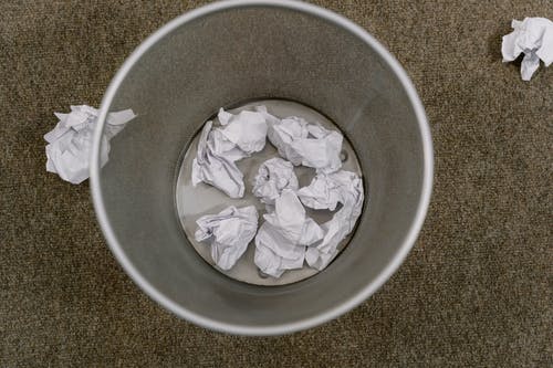 Overhead shot of gray trash can with wads of paper to represent deleting a comment on Instagram. 