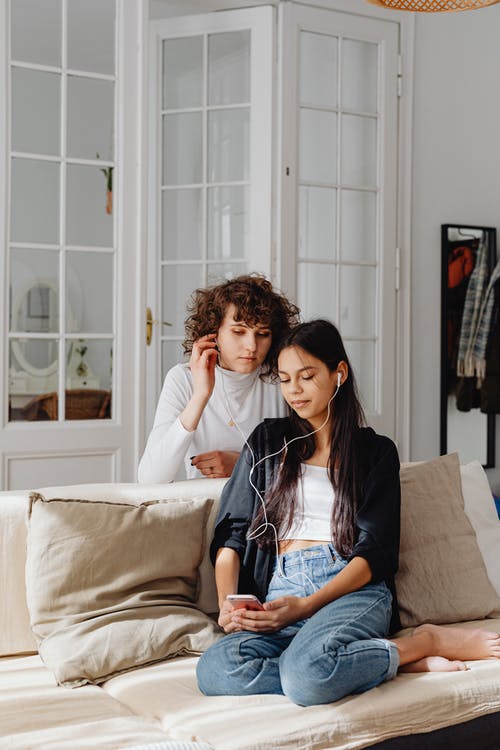 Two people sitting on a beige couch with headphones in looking at a phone to add music to Instagram Story.