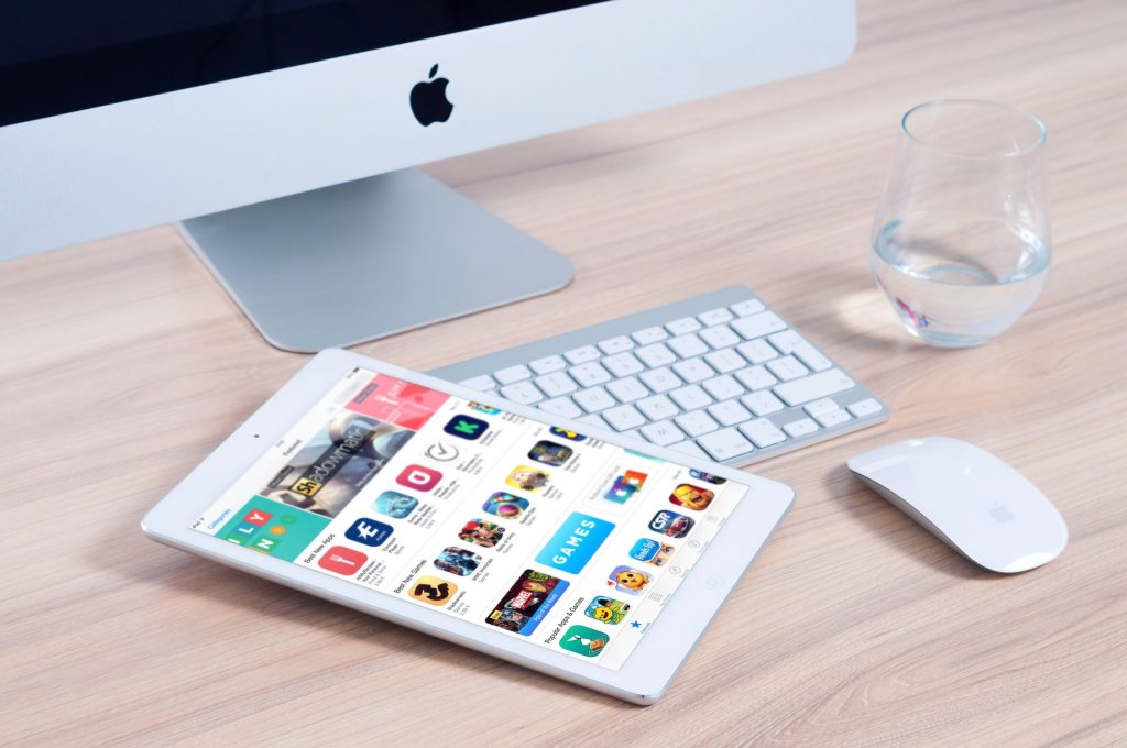 Un Ipad posé sur un clavier, à côté d'une souris, d'un verre d'eau et d'un ordinateur de bureau.