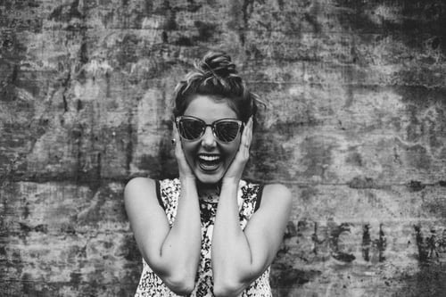 Grayscale image of  a woman covering her ears while laughing to demonstrate how to mute someone on Instagram.