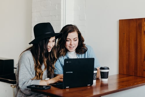 Two women in front of a laptop writing a catchy caption to create interesting Instagram content. 