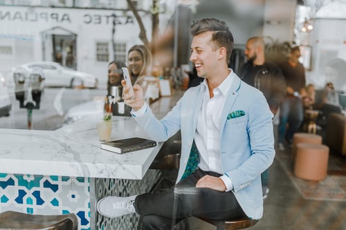 Un hombre sentado en un restaurante, con el teléfono en la mano y mirando los comentarios de un cliente en Instagram. 