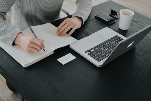 A man sitting in front of a laptop and taking notes on how to create interesting Instagram content. 