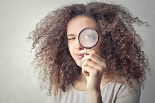 A girl holding a magnifying glass to her eye to demonstrate how to get featured on Instagram’s Explore page. 