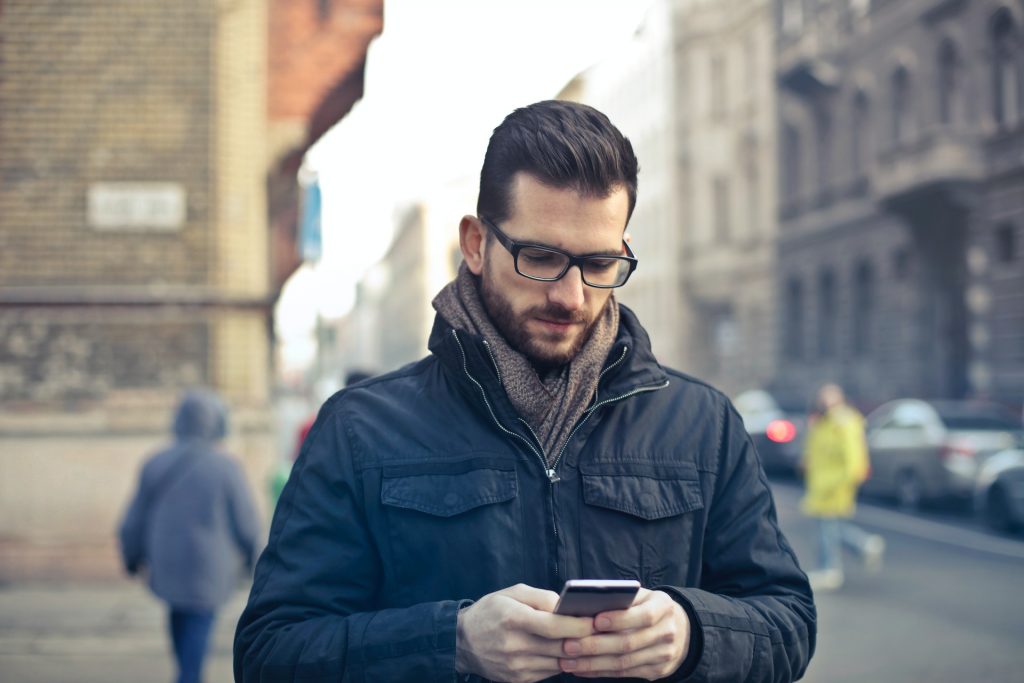 Man standing outside holding a smartphone and learning how to repost a story on Instagram.
