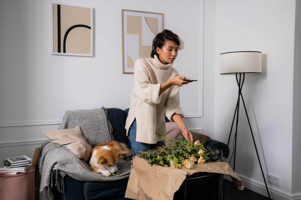 Woman taking picture of flowers on a coffee table and learning how to make a reel on Instagram.