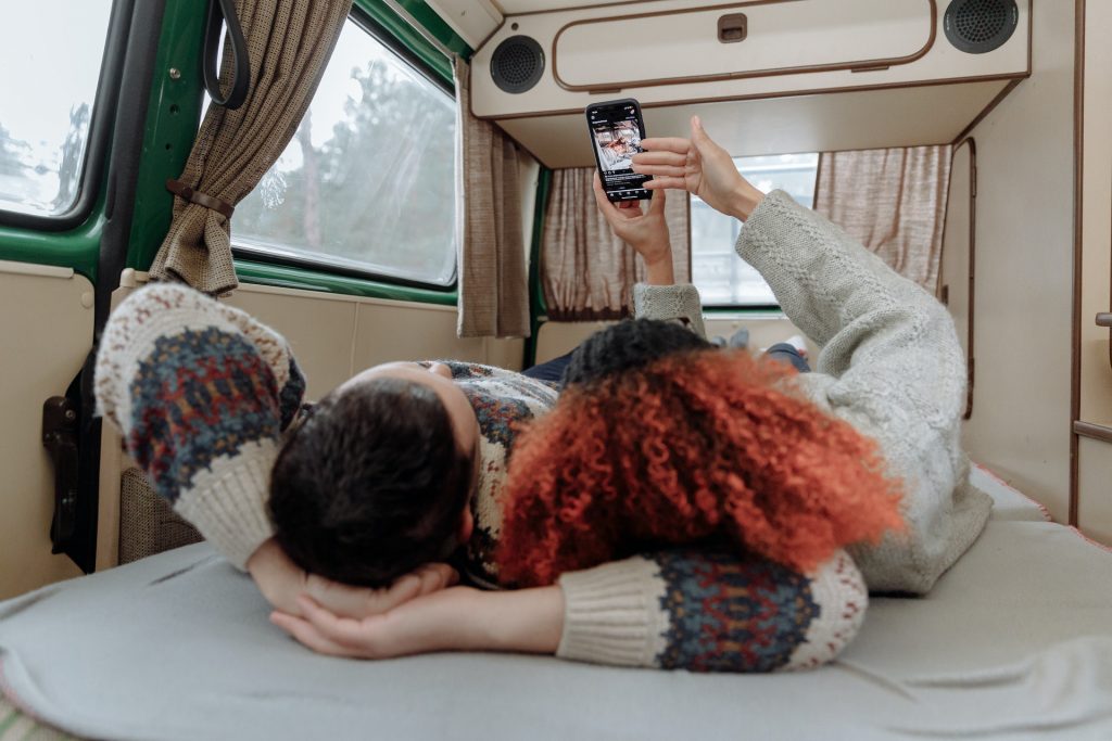 Couple laying on bed in mobile home watching Instagram on a smartphone.