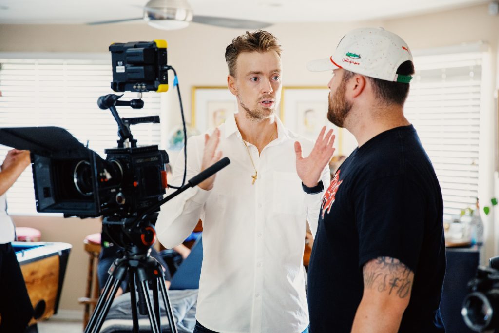 a man talking to another man in a room with a vidoegrapher