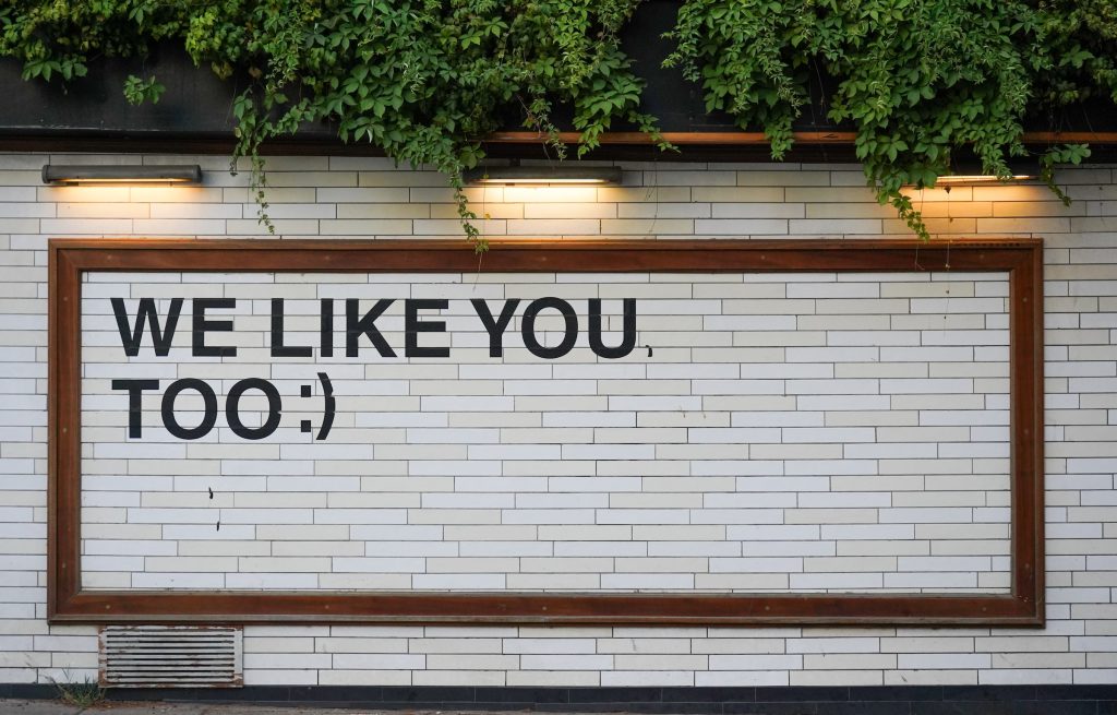 A sign on a white brick wall saying, “We like you, too,” as a response to positive social listening results.
