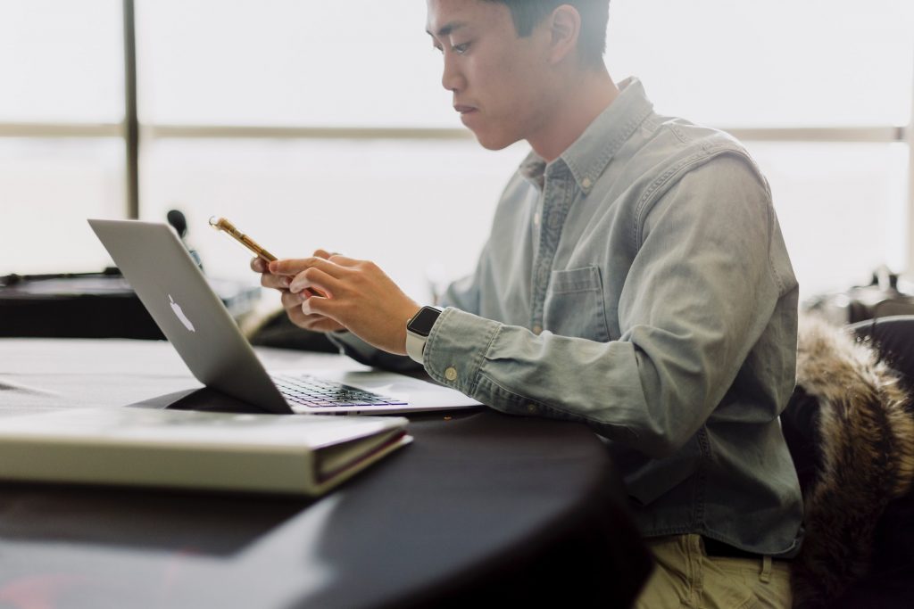 Young man using cell phone and macbook.