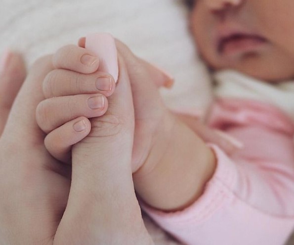 Newborn baby grabbing mother's thumb.