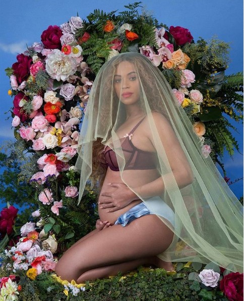 Femme enceinte agenouillée devant des fleurs.