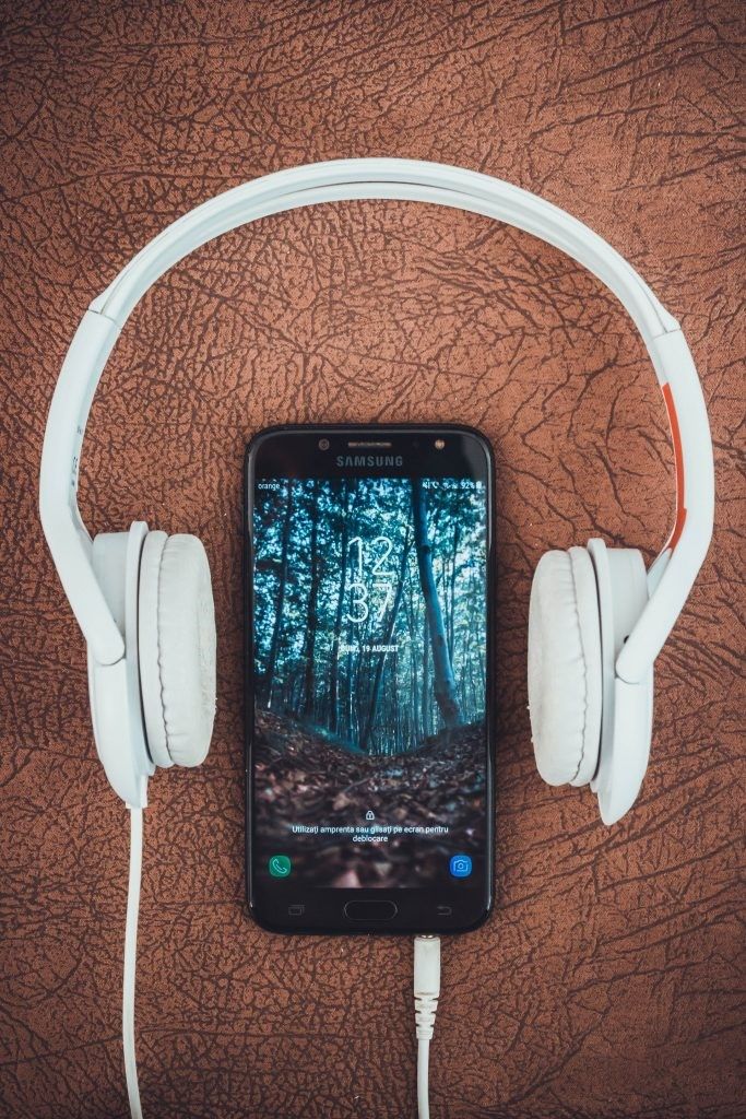 Smartphone laying on table between headphones that are plugged into it.