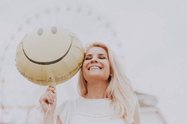 Mulher a sorrir ao lado de um balão com uma cara sorridente.