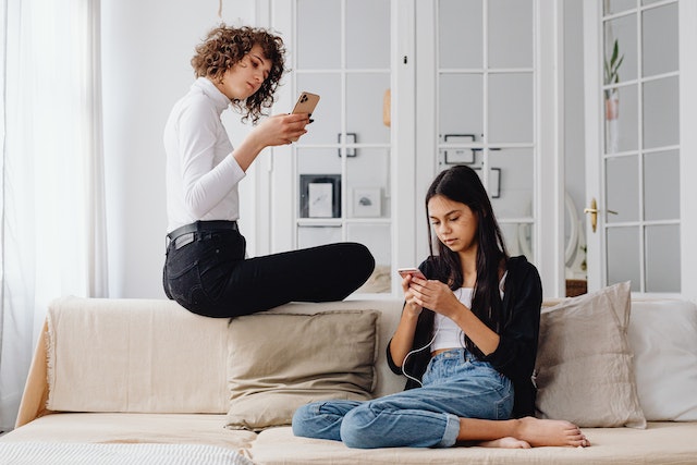 Two women sitting on chairs looking at their smartphones and learning how to repost a story on Instagram.