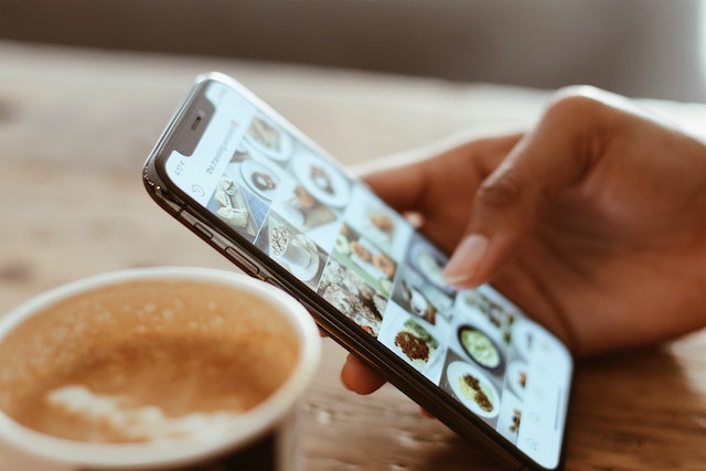 Personne tenant un smartphone ouvert sur l'application Instagram sur une table avec une tasse de café.