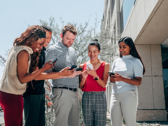 Grup de oameni care se uită în jos la smartphone-urile lor pentru a învăța cum să facă o rolă pe Instagram.