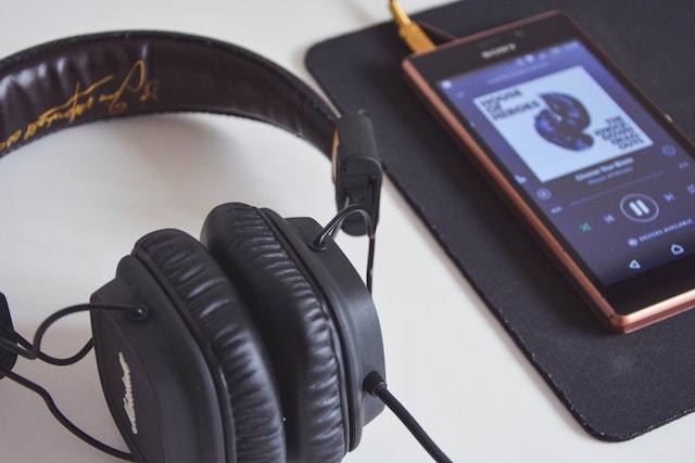 Foto de unos auriculares junto a un teléfono mientras se reproduce música.