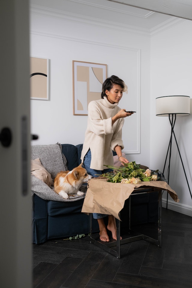 Mujeres de pie en un salón tomando una foto de flores sobre una mesa de café.