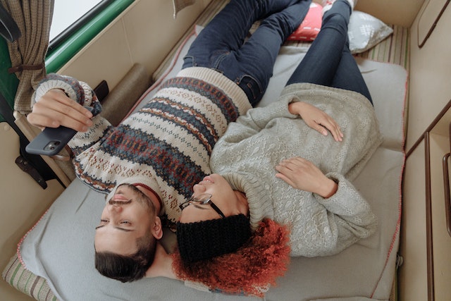Casal deitado na cama numa casa móvel a ver Instagram num smartphone.