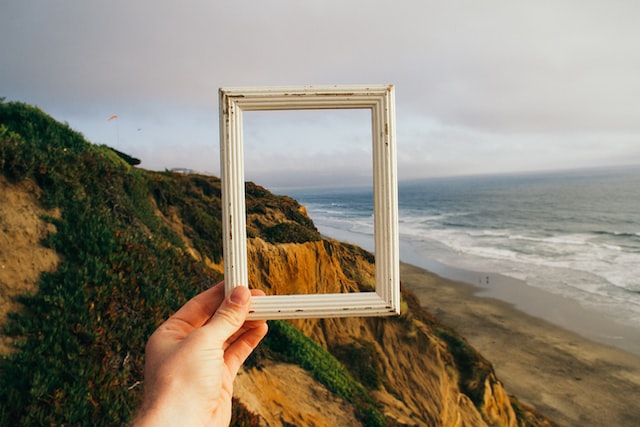 Person holding a photo frame over a view of the ocean.