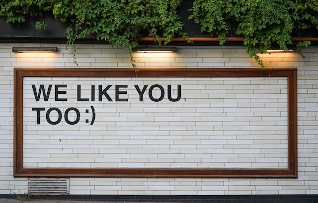 Um sinal numa parede de tijolo branco a dizer: "Também gostamos de si", como resposta a resultados positivos de escuta social. 