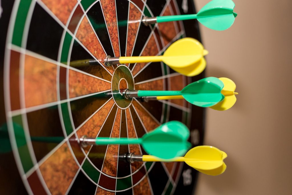 Dartboard with yellow and green darts. 