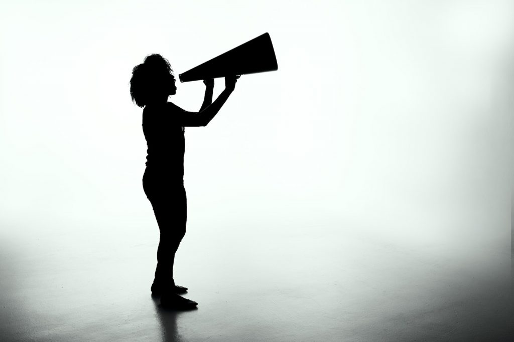 patrick-fore-5YU0uZh43Bk-unsplash | Path Social A black silhouette of a woman shouting into a megaphone against a white background.