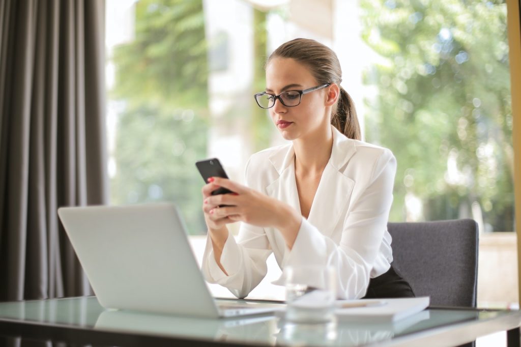 pexels-andrea-piacquadio-3761520 | Path Social Vrouw zit achter haar bureau voor een laptop en gebruikt een mobiele telefoon.