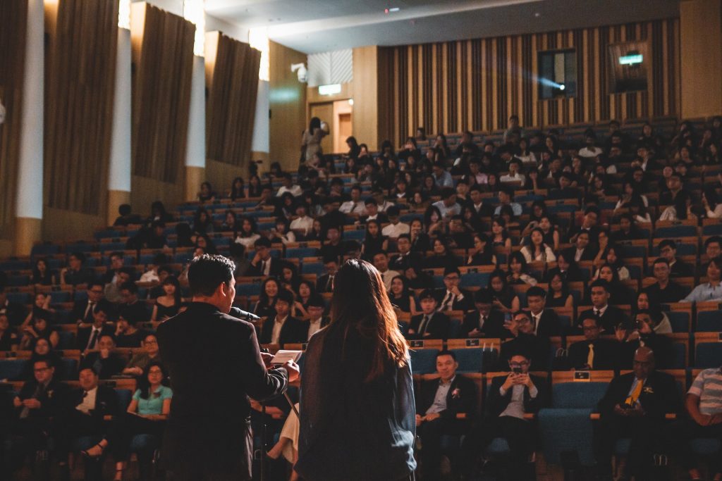 Two people speaking in front of a bit audience.