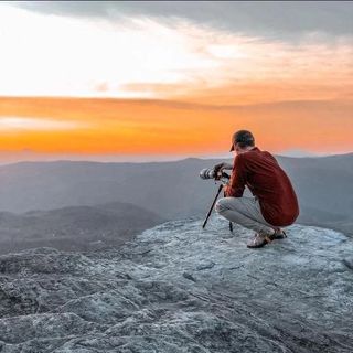 a man sitting on a rock with a camera on a tripod