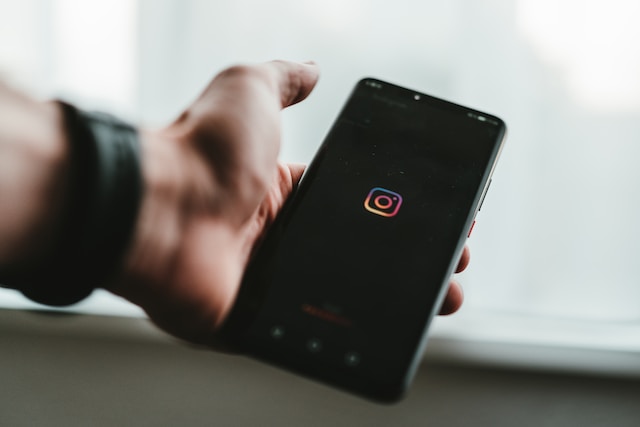 A hand holding a black phone displaying the Instagram logo.