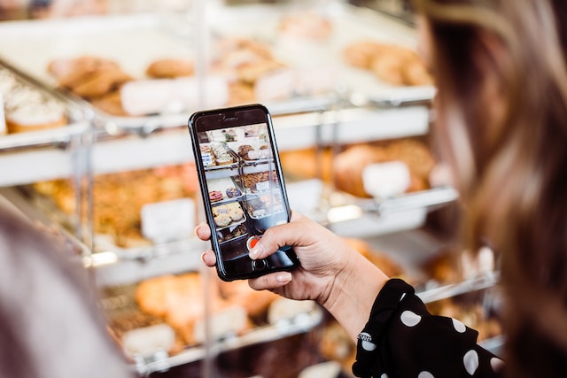 O clientă fotografiază produsele de patiserie cu telefonul ei.