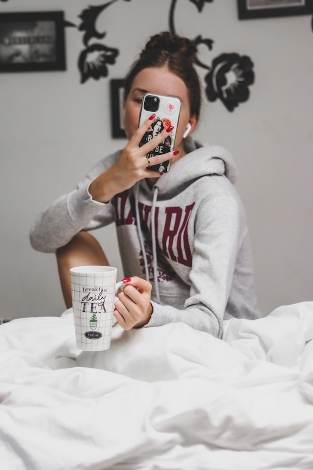 An Instagram model holding a mug taking a selfie for content.