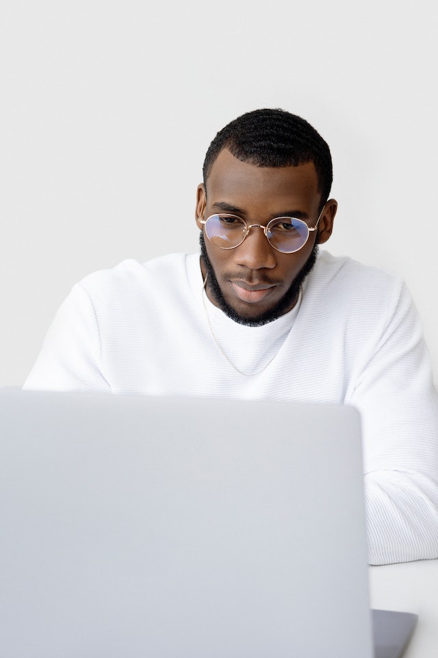 Un homme en blanc regarde attentivement son ordinateur portable.