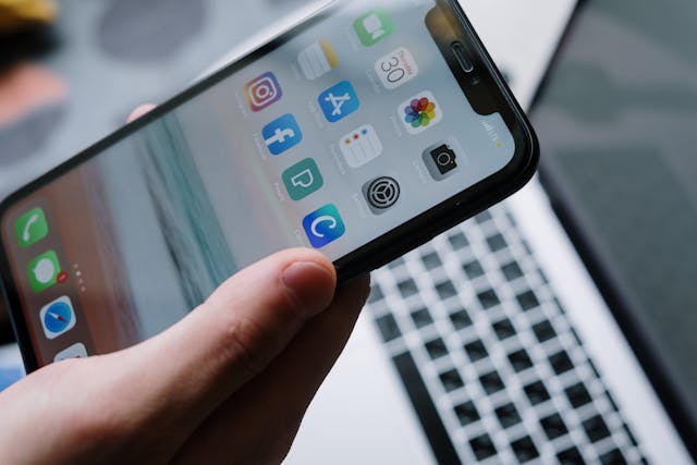 pexels-cottonbro-5054355 | Path Social Persona sosteniendo un smartphone encima de un portátil con aplicaciones de redes sociales en la pantalla.
