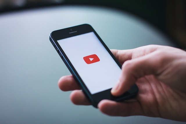 Hand holds an iPhone with the YouTube app displayed