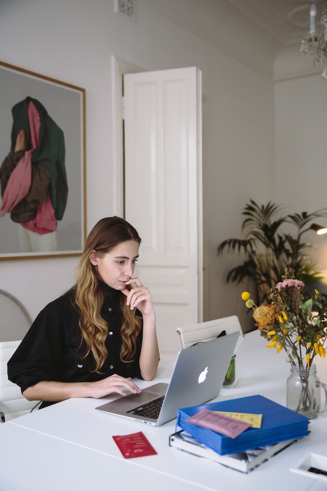 Woman sits around a table, looking intently at a computer screen.