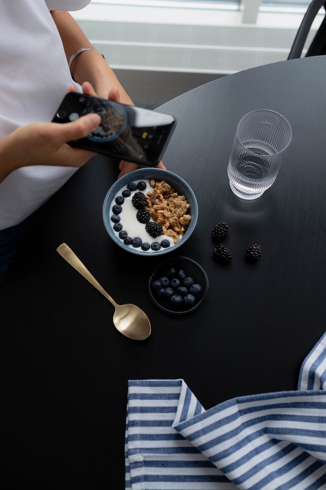 Mulher a tirar uma fotografia de uma taça de granola e mirtilos