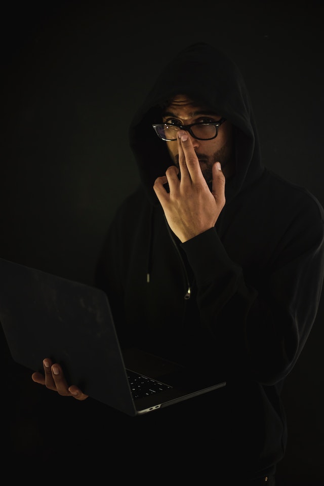 Un hombre con capucha y gafas sostiene un ordenador portátil.