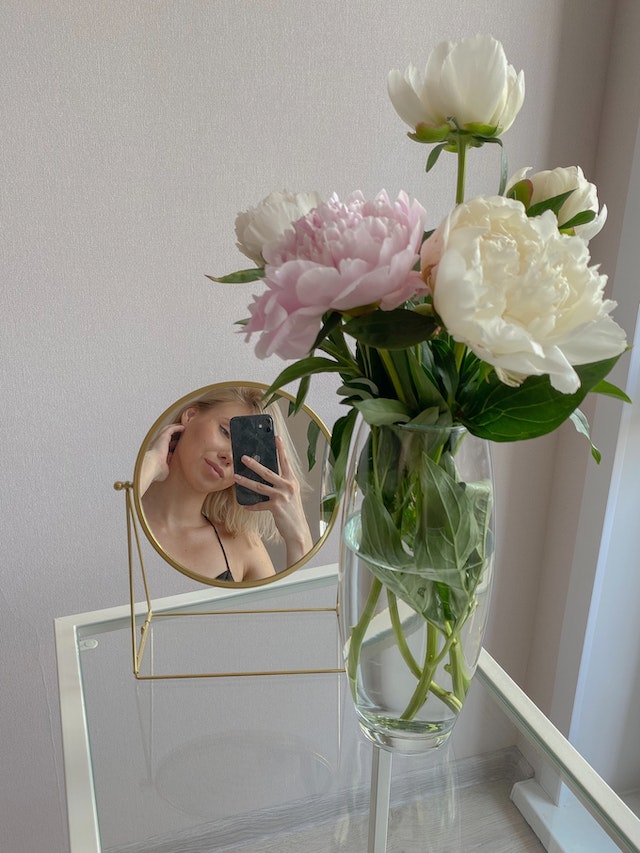 Een minimalistische spiegel selfie met witte en roze bloemen op een heldere glazen tafel