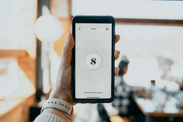 Persona sosteniendo un teléfono con un signo de dólar en la pantalla que representa los ingresos de una modelo de Instagram.