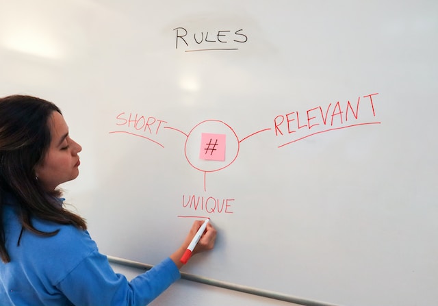 walls-io-ZRmSqNfrtGw-unsplash | Path Social A woman writing on a whiteboard brainstorming hashtag strategy.