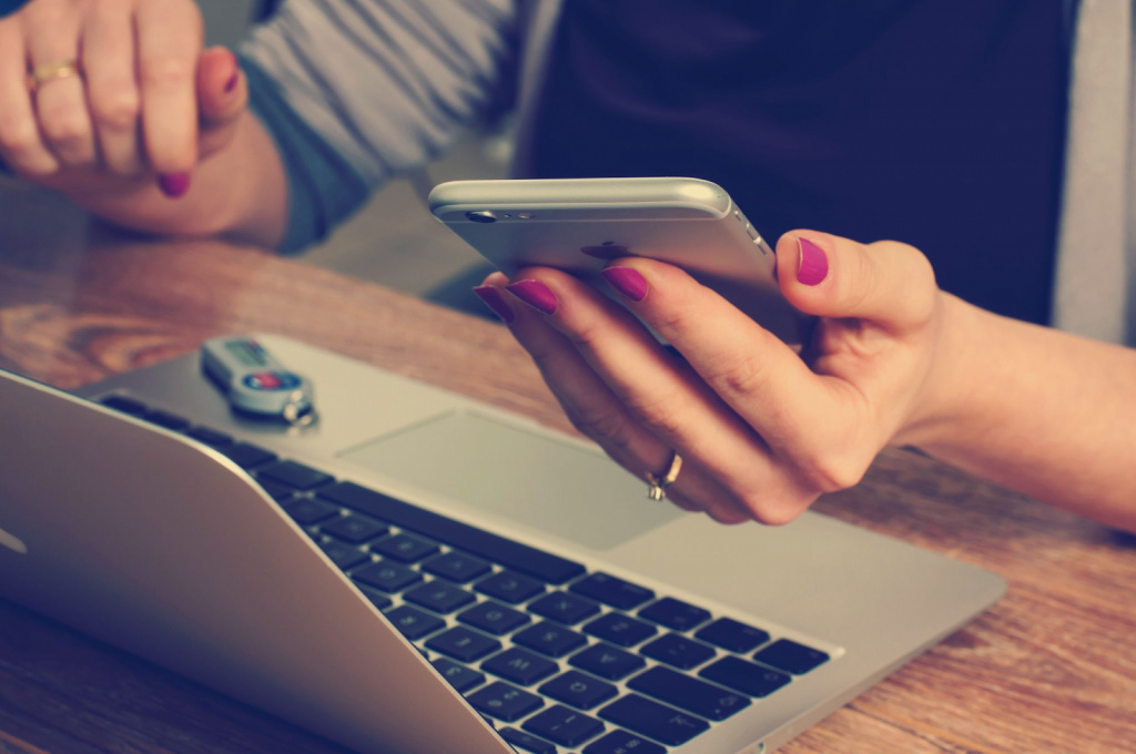 Une personne assise à son bureau avec un MacBook et un iPhone en train de créer des couvertures pour un compte d'entreprise.