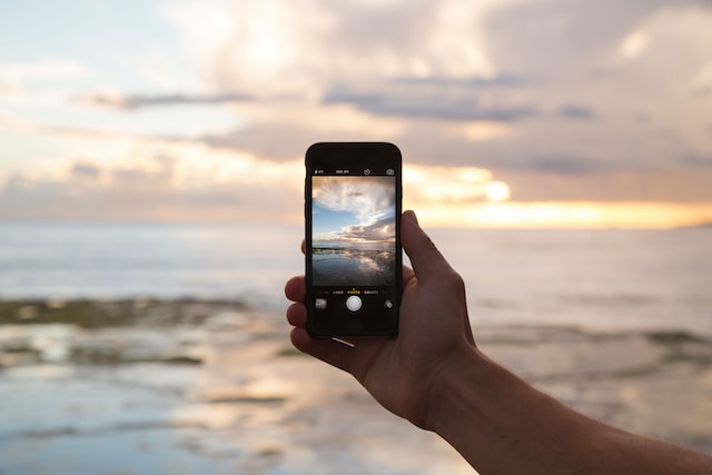 Alguém com o telemóvel na mão a tirar uma fotografia da praia para o Instagram.